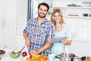 Young couple chopping vegetable and holding digital tablet