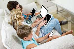 Family using various technologies while sitting on sofa