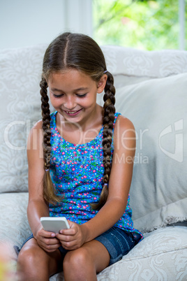 Girl using mobile phone while sitting on sofa at home