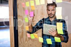 Man using digital tablet while writing on sticky notes