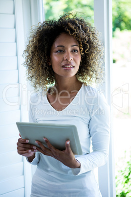 Thoughtful woman standing near the window and using a digital ta