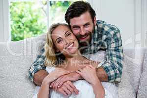 Husband embracing wife from behind against window