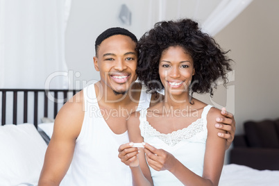 Happy couple looking at pregnancy test on bed