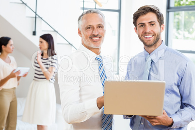 Two businessmen are smiling, posing and holding a laptop