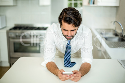 Businessman using cellphone at table in kitchen