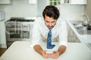 Businessman using cellphone at table in kitchen