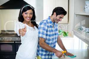 Woman showing her thumbs up while man cleaning the kitchen