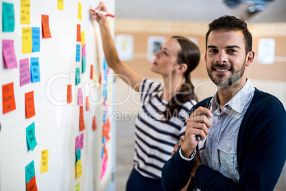 Young man smiling at camera while colleague writing on white boa