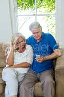 Serious senior couple using mobile phone while sitting on sofa