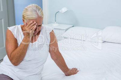 Upset senior woman touching head at home