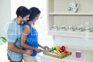 Man embracing woman while chopping vegetables in kitchen