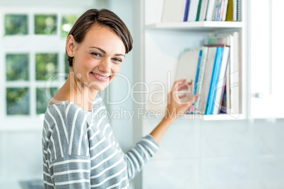 Beautiful woman picking book from cabinet at home