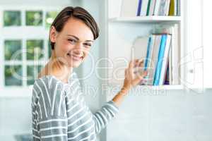 Beautiful woman picking book from cabinet at home