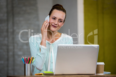 Woman talking on mobile phone while using laptop