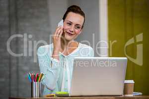 Woman talking on mobile phone while using laptop