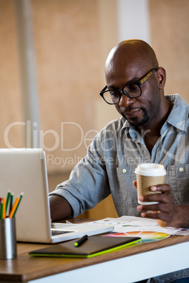 Graphic designer using laptop in office and holding a coffee