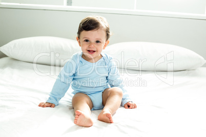 Cute baby boy sitting on bed at home