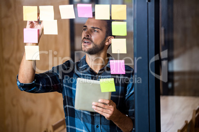 Man using digital tablet while writing on sticky notes