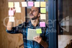 Man using digital tablet while writing on sticky notes