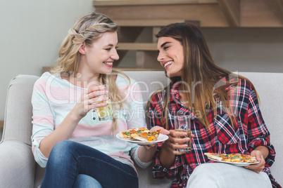 Two beautiful woman sitting on sofa and having pizza