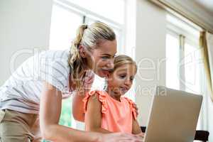 Smiling mother with daughter using laptop at home