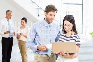 Businessman holding coffee cup and a colleague using laptop