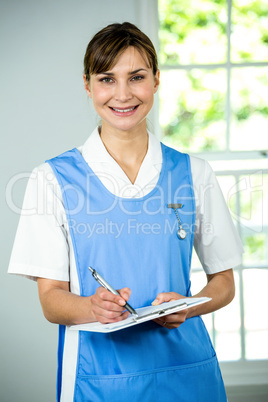 Portrait of smiling nurse writing on clipboard