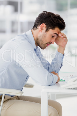 Frustrated businessman sitting on desk with hand on head