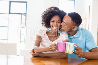 Man kissing woman while toasting coffee mug
