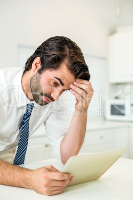 Tensed businessman looking at digital tablet by table