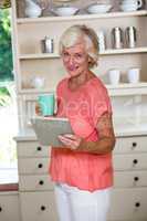 Senior woman using digital tablet while having coffee in kitchen
