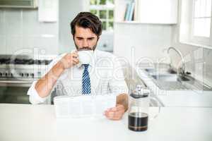 Businessman reading newspaper while drinking coffee at table