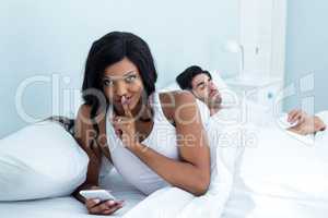 Woman checking her mobile phone while sleeping on bed