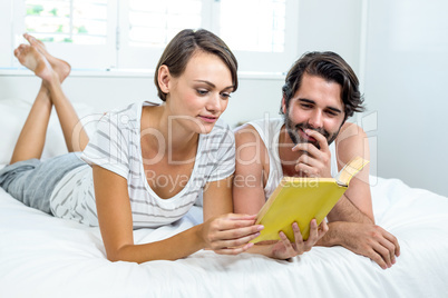 Couple reading book while lying on bed