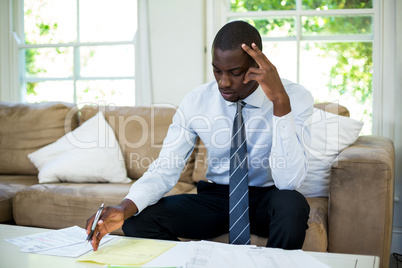 Tensed man sitting on sofa and accounting the bills