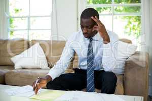 Tensed man sitting on sofa and accounting the bills