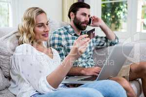 Woman holding debit card by man talking on phone with laptop