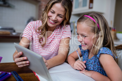 Mother using a digital tablet while helping daughter with her ho