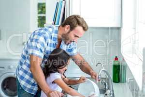 Daughter helping father in washing utensils