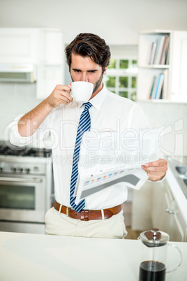 Businessman drinking coffee while reading newspaper at table