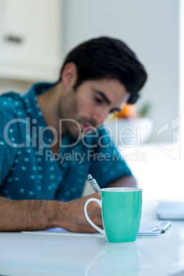 Man writing on clipboard with coffee mug on table