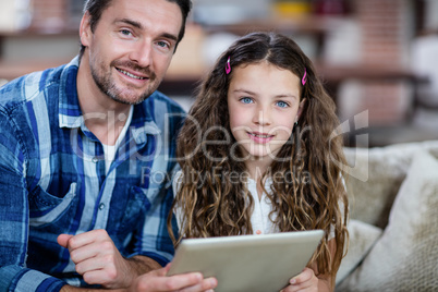 Portrait of father and daughter using digital tablet in living r