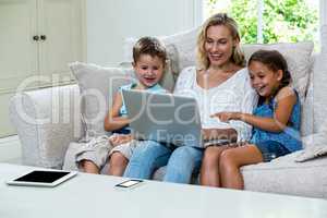 Cheerful children and mother using laptop on sofa