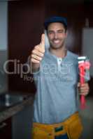 Cheerful man showing thumbs up while holding pipe wrench