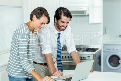 Couple looking in laptop while standing by table in kitchen