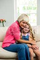 Smiling granny and girl hugging while sitting on sofa