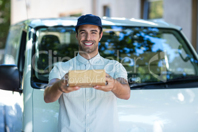 Portrait of cheerful delivery man giving cardboard box