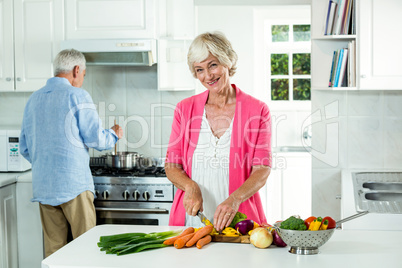 Portrait of happy senior woman cutting vegetables