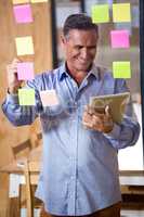 Man using digital tablet while writing on sticky notes