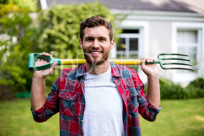 Smiling man carrying rake while standing in yard